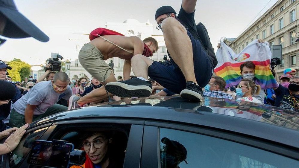 Photo from the movie: two young men on a car roof. Behind a car a crowd of people - it looks like a demonstration.