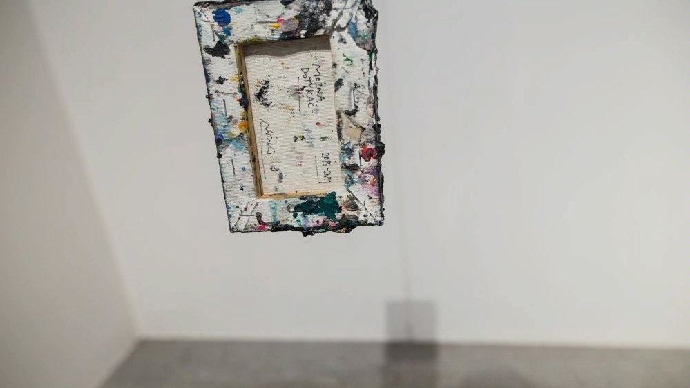 One of the works from exhibition - colourful picture frame with a picture with some inscriptions. White wall as a background.