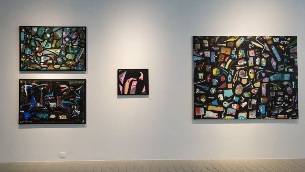 Four colourful abstract pictures on a white wall.