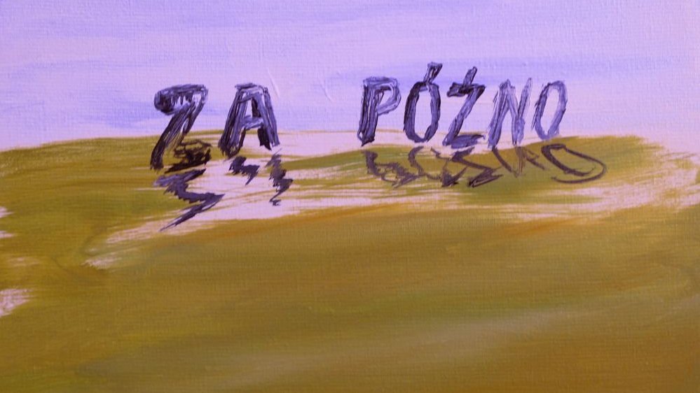 One of the works from the exhibition.The caption "Za późno" on a green field, blue sky behind it.