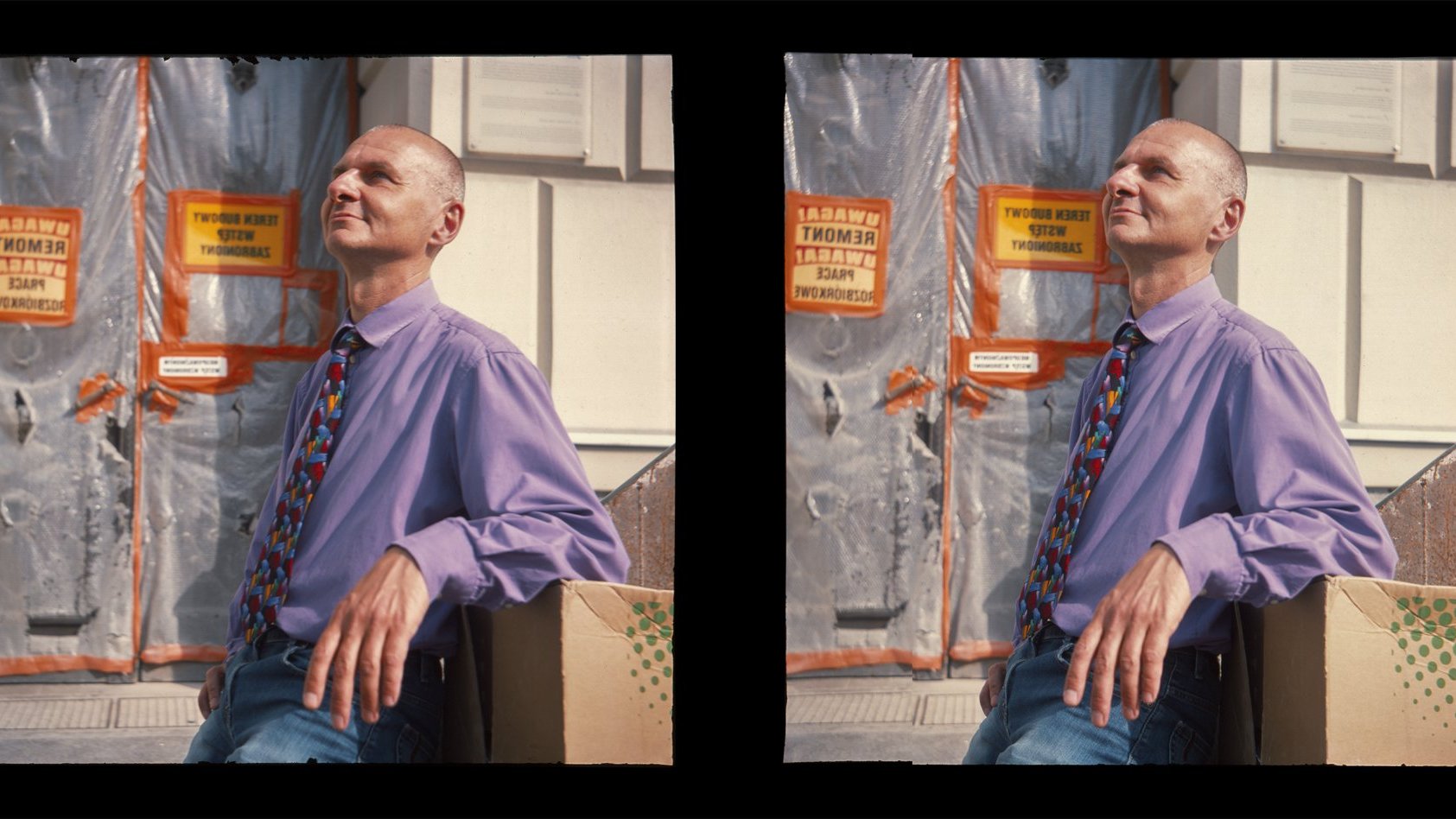 Stereoscopic photograph presenting a man in a light violet shirt and colourful tie, who is leaning against a carton box and looking up; as a background a fragment of a wall being restored.