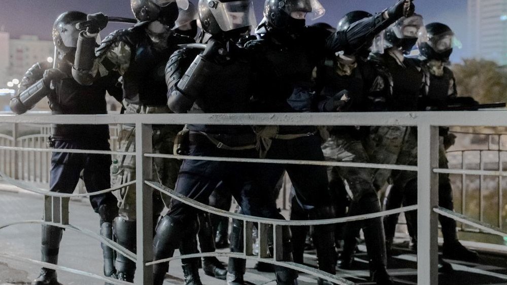 Photo of a group of policemen in black garments with helmets on teir heads, holding clubs in their hands.