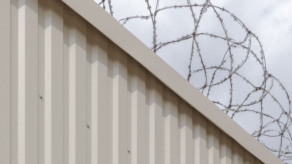 Photo of a fragment of the high wall with barbed wire on it.