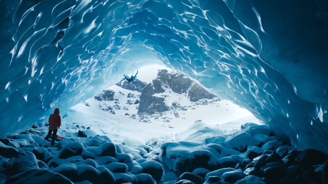 Picture from the movie - mountain landscape in blue and white colours and two persons - one is climbing and one standing on the rocks.