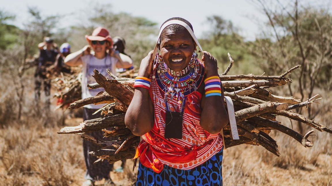 Photo from the movie - women colourfully dressed, carrying firewood on their backs.