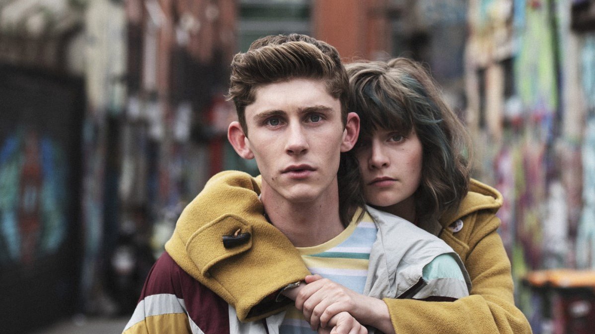 Photo of a couple - young woman who is behind a young man and is embracing him with her arms