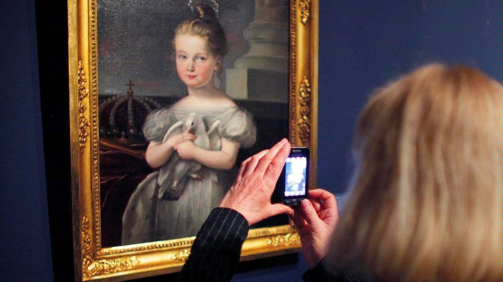 Photo of a woman taking a shot of the picture hanging on the wall - grafika artykułu