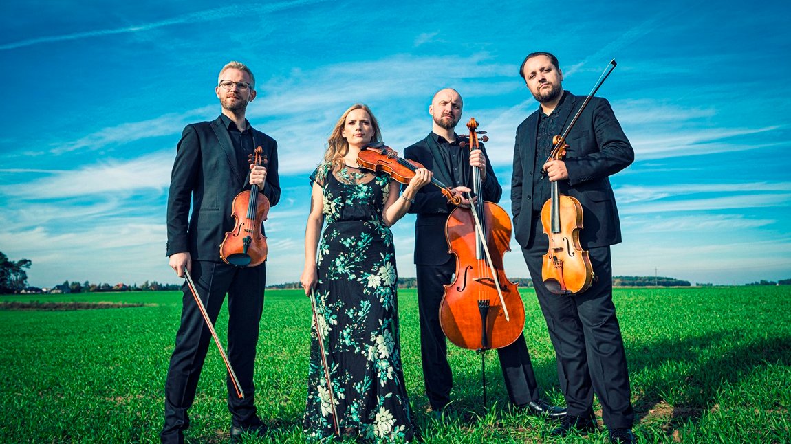 Photo of the Meccore String Quartet members: one woman and three men holding their musica instruments and standing on the grass. Blue sky as the background. - grafika artykułu