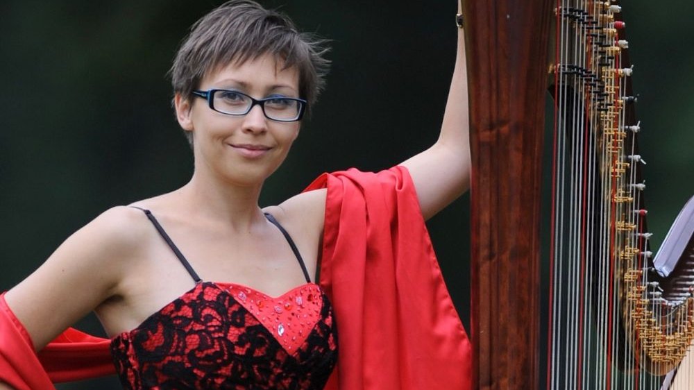 Photo of the artist - a woman standing and holding the harp.