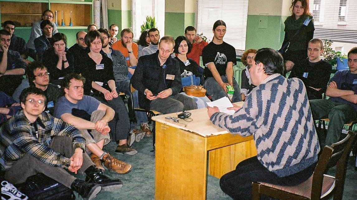 A group of people sitting and listening to the lecture in a classroom. In the foreground a man sitting at the desk, holding papers in his hands.