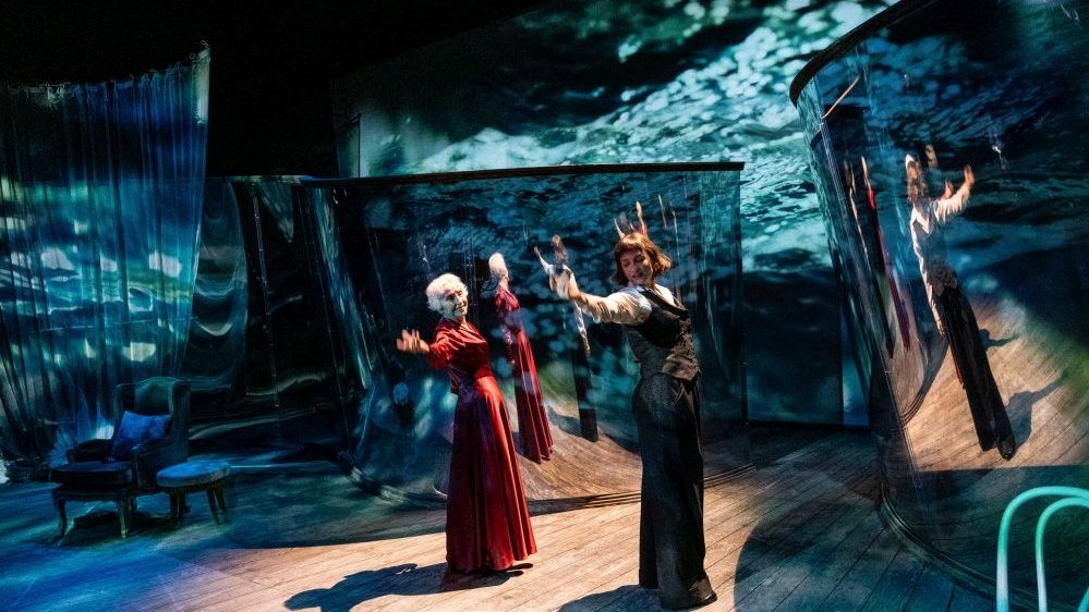 A scene from a performance - two actresses on stage, blue elements of the scenography.