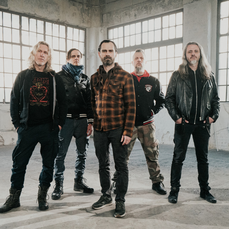 Photograph of the band: 5 men standing inside of empty factory hall with big windows - grafika artykułu