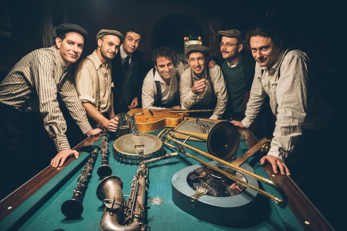 Photo of the band - seven men standing at the billiard table, on which various musical instruments are placed. - grafika artykułu