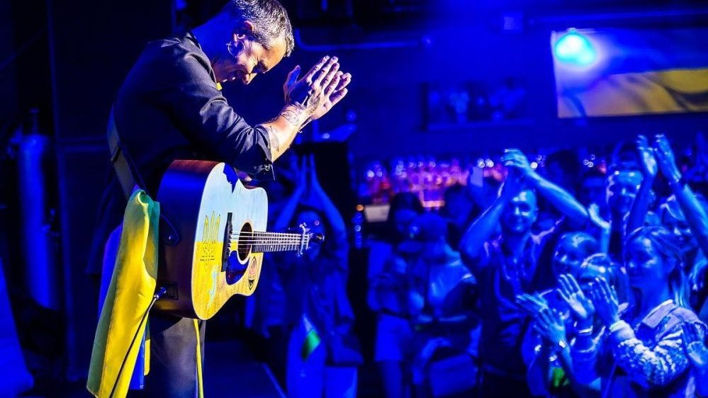 Photo of Sergiy Babkin with the guitar performing on stage; on the right - people who clap their hands.