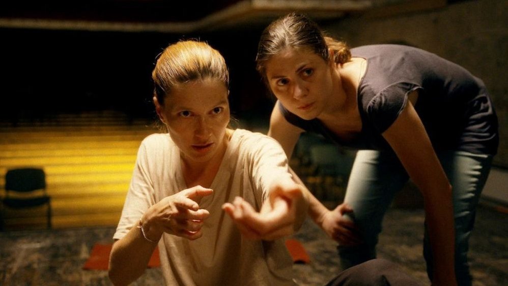 Photo of two women. Both women are looking at something, one of them is pointing something with her hands, both of them are looking in the same direction.