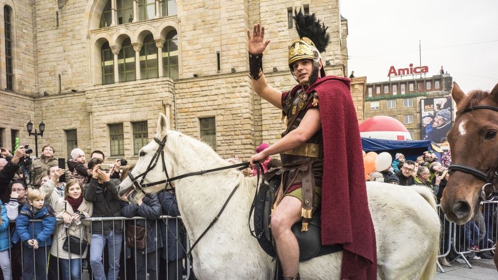 Photo from one of the previous St. Martin parade: picture of a men dressed as St. Martin, sitting on a horse and greeting people. People watching the show in the background.