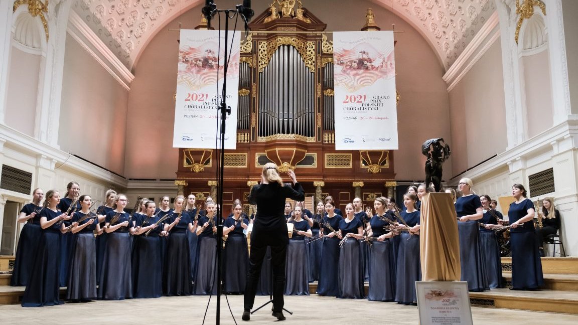 Picture of the choir performing on a stage of AMU Auditorium. Pipe organ in the background.