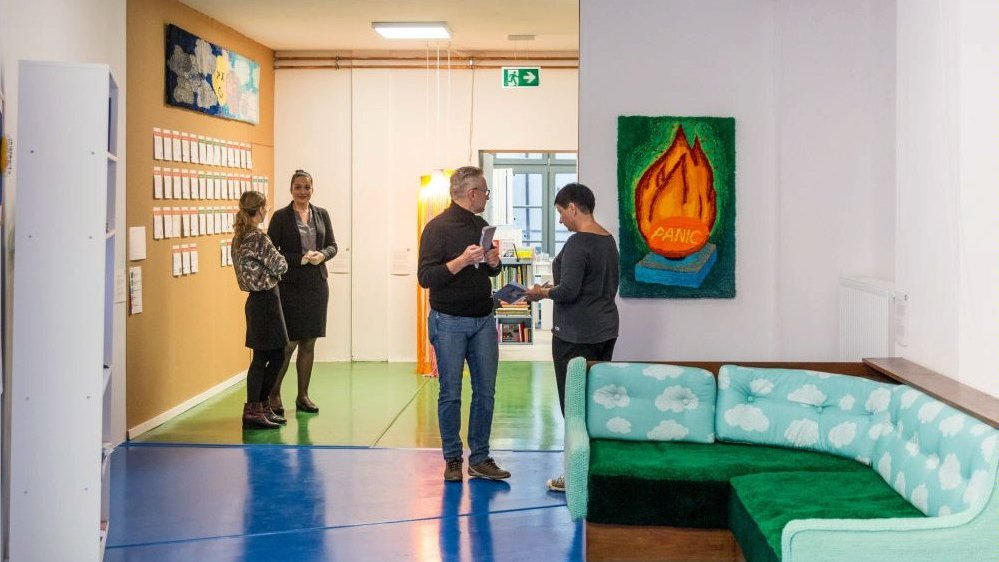 Photo of one of the gallery's halls with some exhibition works and people watching them.