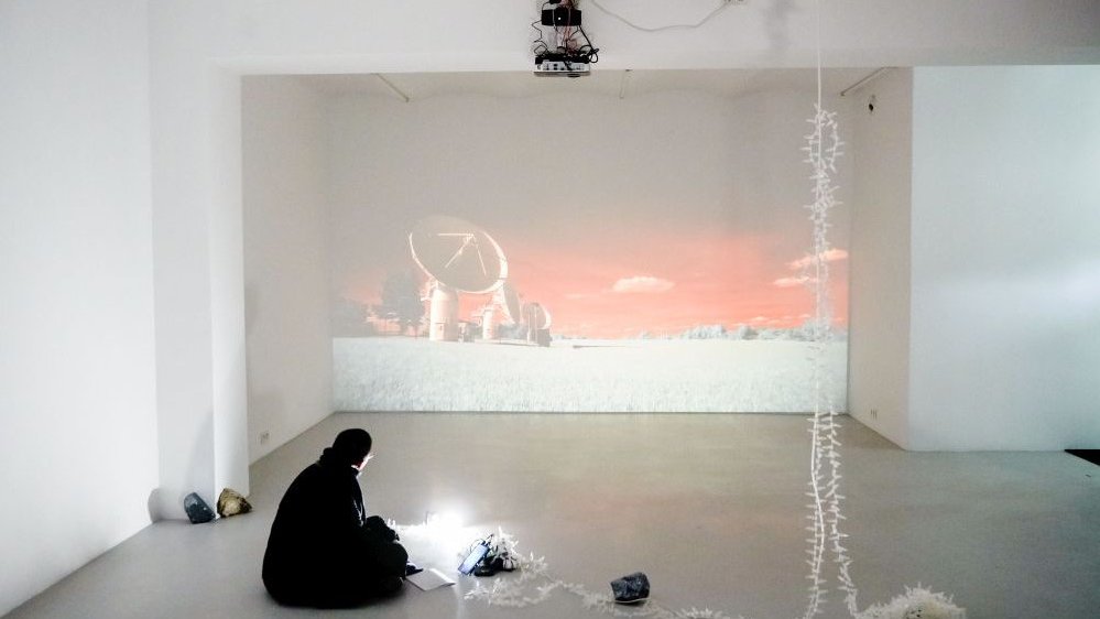 Exhibition hall: a picture of a radar in an open space displayed on a wall and a man sitting in front of the screen and watching it.