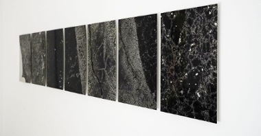 Seven abstract pictures in black and white colours on a wall.