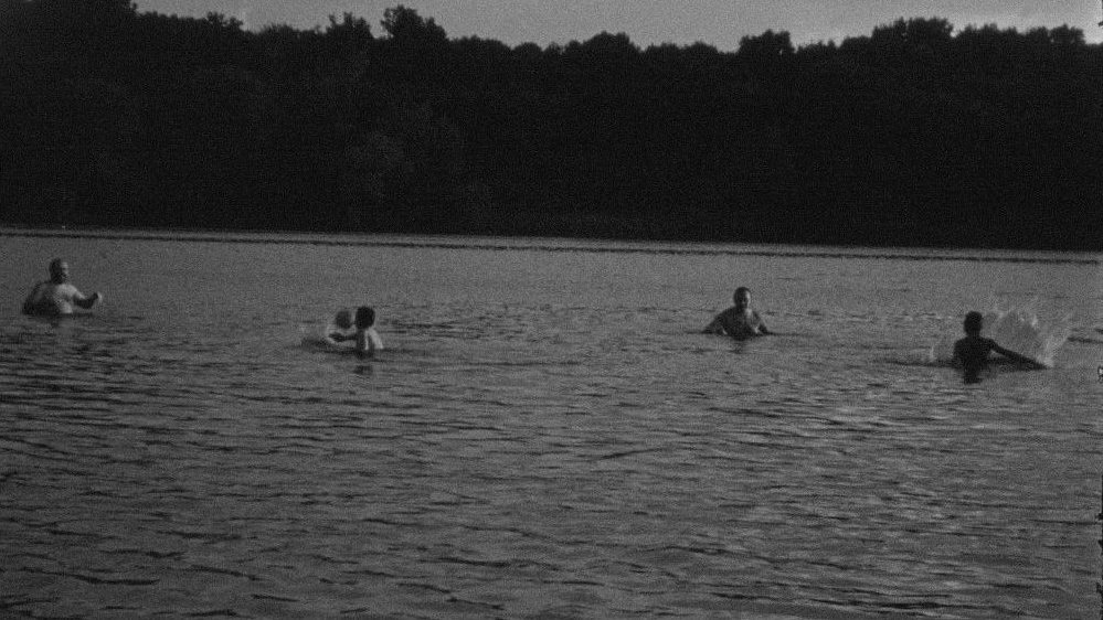 One of the exhibition works - black and white picture of a few people in a lake or river. Forest as a background.