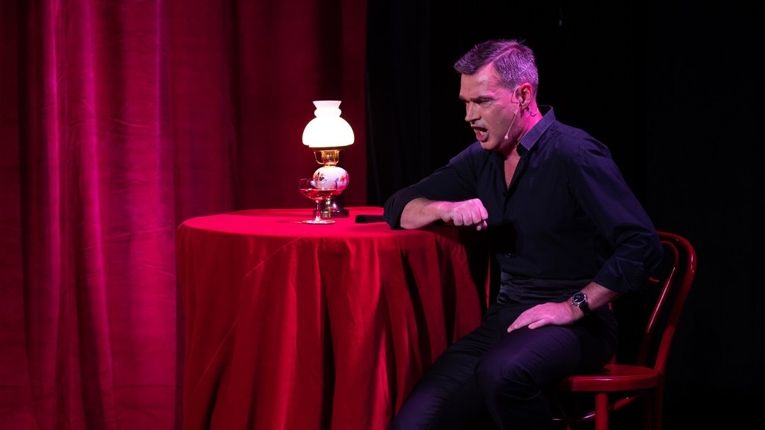 Photo of a singing man who is sitting at the table.