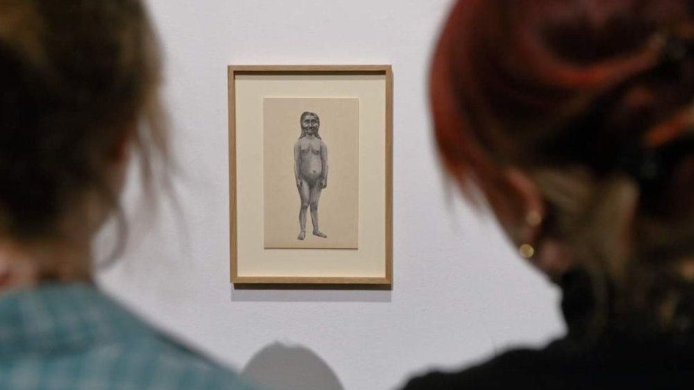 Photo of one of the exhibition works hanging on the wall and two women looking at it. - grafika artykułu