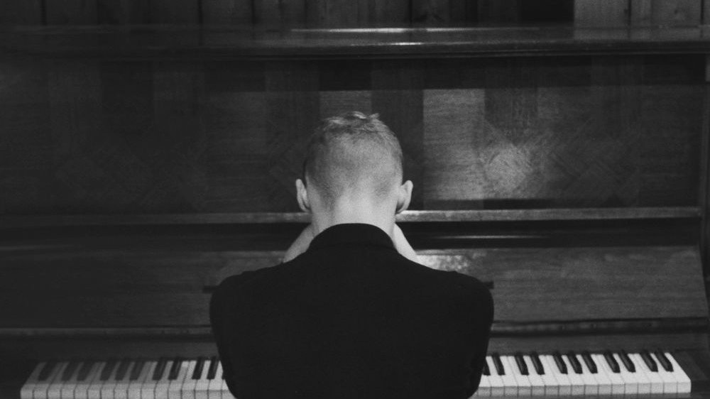 Black and white photo of Igor Herbut, who sits at the piano back to the camera. - grafika artykułu