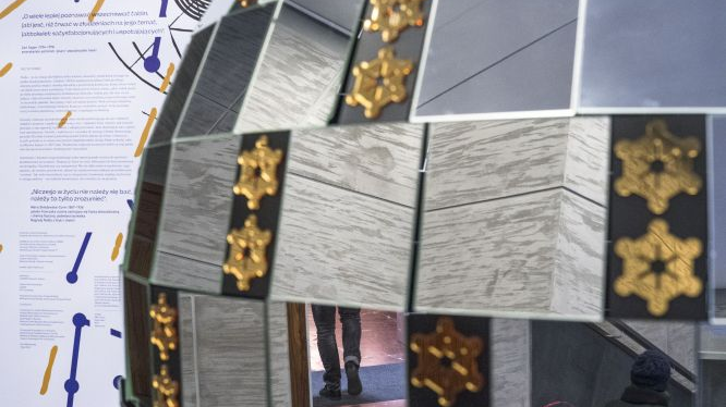 A model of a sphere made of silver and mirrorlike squares. In the background a chart with information about the exposition.