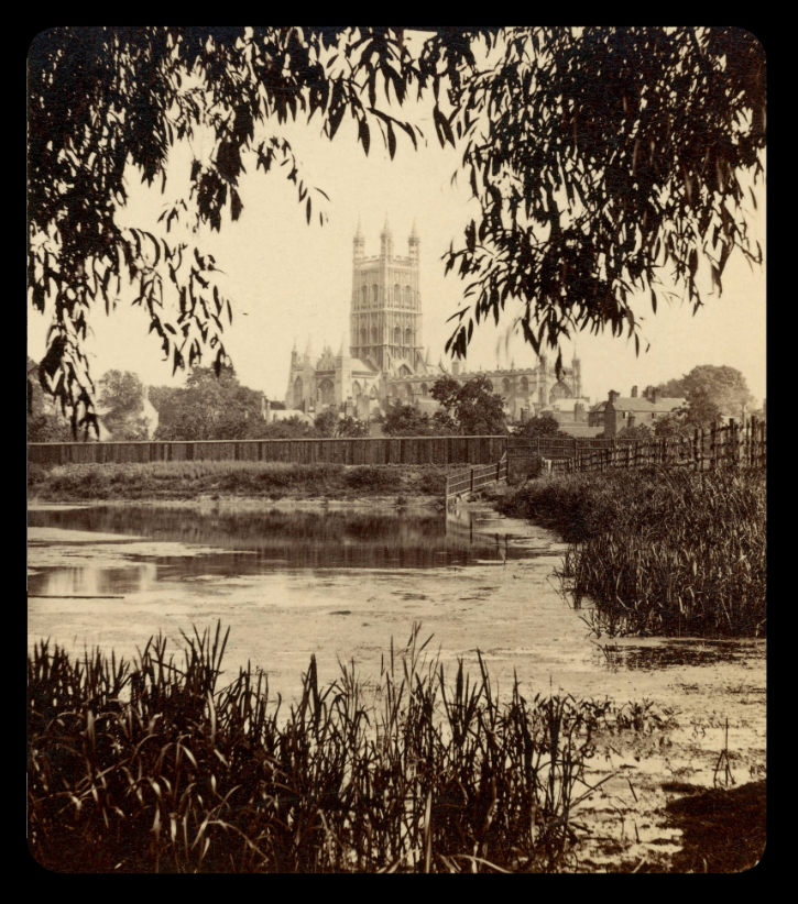 Sepia photograph of the Gloucester Cathedral, which is in the background. In the foreground a lake or a river with some water plants. - grafika artykułu