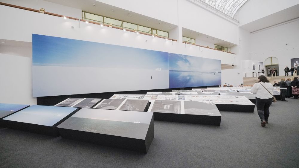 Photo of the exhibition hall with two big pictures hanging on the wall and other pictures displayed on low expositors.