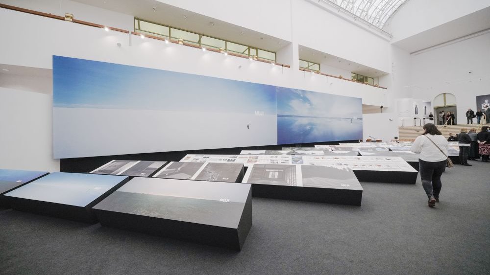 Photo of the exhibition hall with two big pictures hanging on the wall and other pictures displayed on low expositors. - grafika artykułu