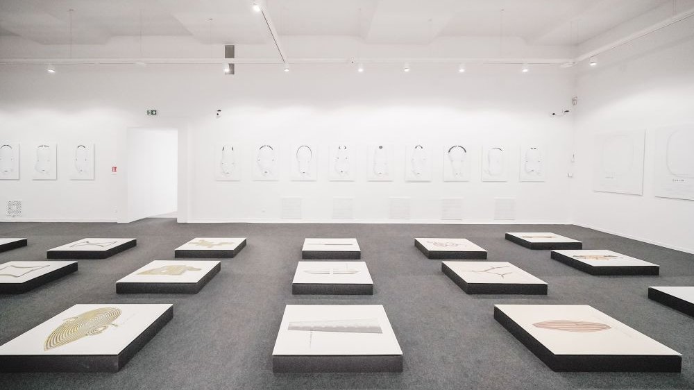 Photo of the exhibition hall with some works displayed on the floor. In the background pictures hanging on the wall.