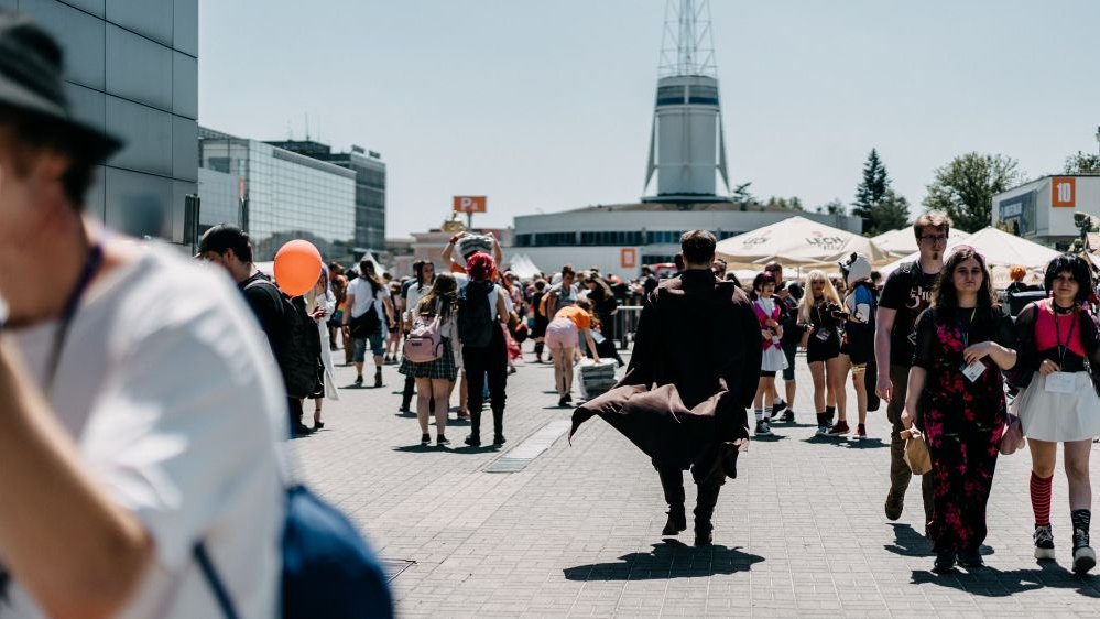 Photo of Poznań's fairgrounds: people walking around and some buildings as a background.