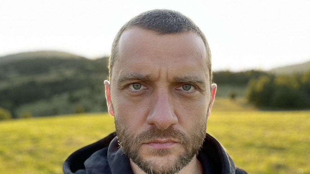 Photo of Aleksander Nowak's face, which looks worried. Green meadow as a background.