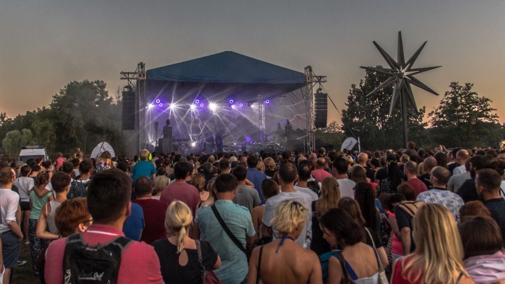 Photo of the audience that is looking at illuminated outdoor stage where the concert is taking place.