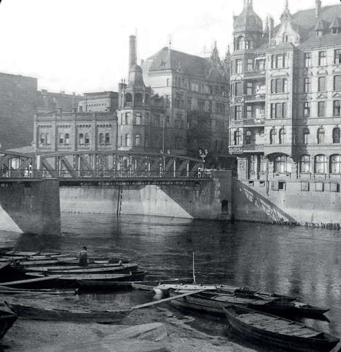 Black and white photo of the river, a few boats, the bridge and buildings along the river. - grafika artykułu