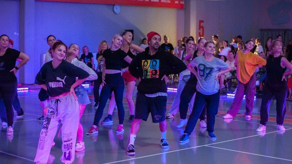 A group of dancing people, all in similar poses. Photo in blue colours. - grafika artykułu