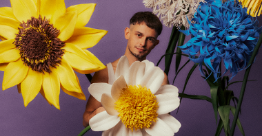 A young man standing behind and among big flowers.