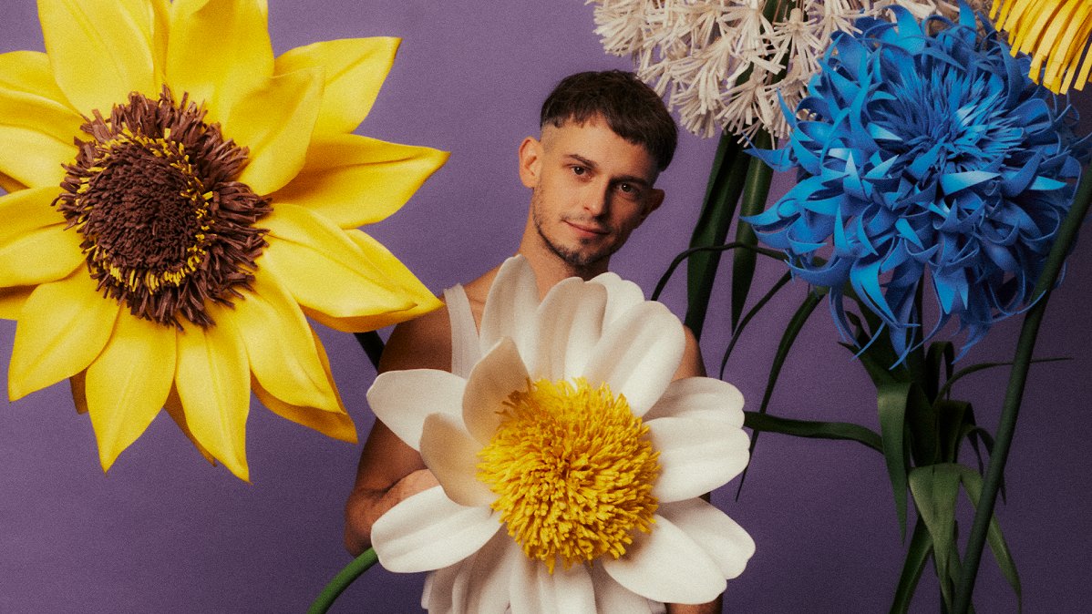 A young man standing behind and among big flowers.