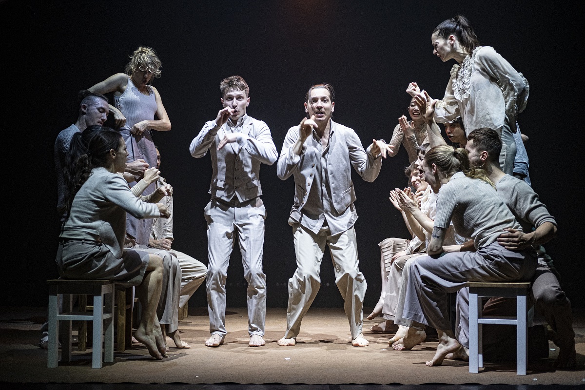 Photo of a group of dancers, some of them standing and some of them sitting on stools. - grafika artykułu