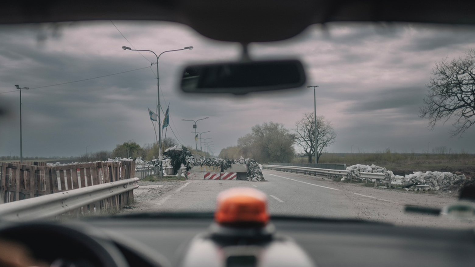 View from inside of the car onto a street full of rubble and bags. Cloudy weather.