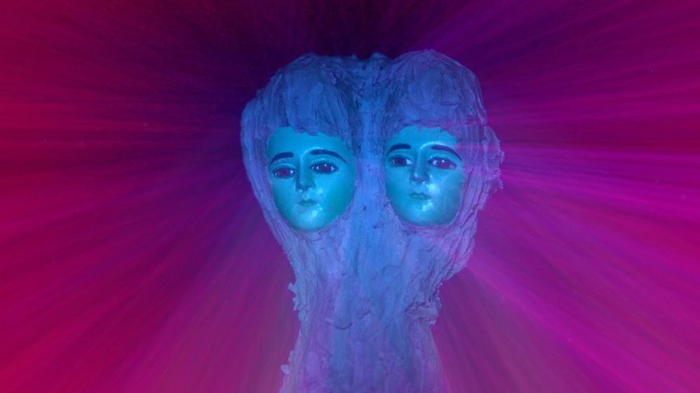 Faces of two dolls with long blue hair, connected to each other. Purple and burgundy background.