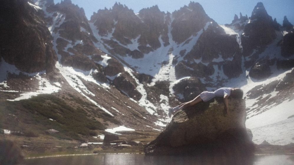 Mountain landscape on a sunny day. On a rock, face down, a woman dressed in a short dress is lying.