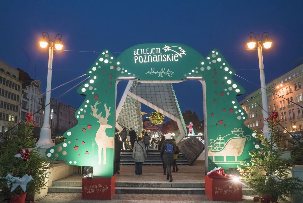 The green gate through which people enter the fair. A fountain is visible behind it. - grafika artykułu