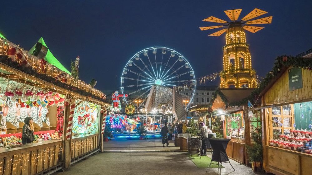 Colorful, brightly lit stands with goods, a Ferris wheel and a wooden tower with a windmill in the background