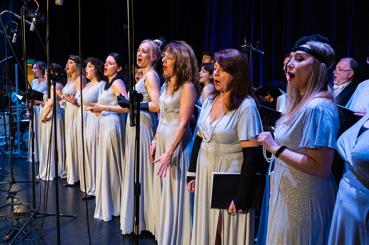Photo from the concert: women in long white-silver dresses singing on stage. - grafika artykułu