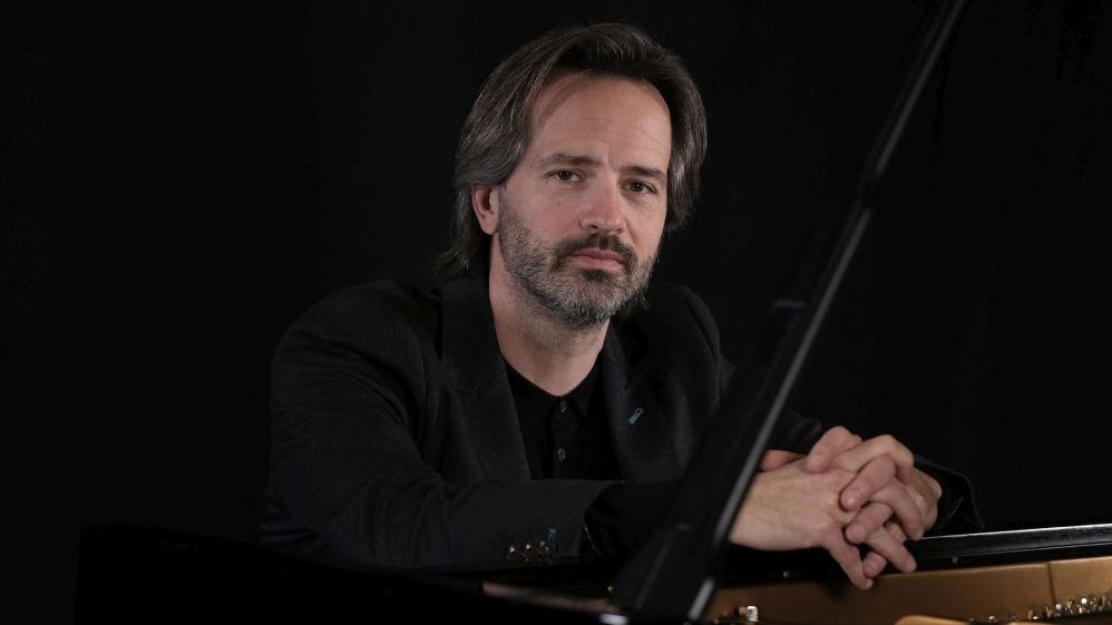 A middle-aged man, dressed in black, sitting at the piano.