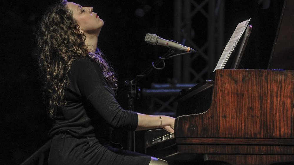 A woman sitting and playing at the piano, with her face up and closed eyes.