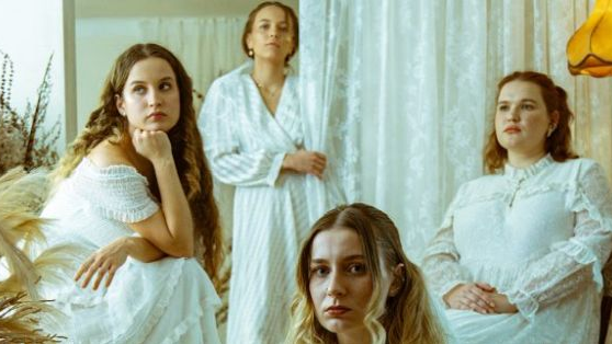 Four young women, dressed in white dresses. Each of them looks in a different direction.